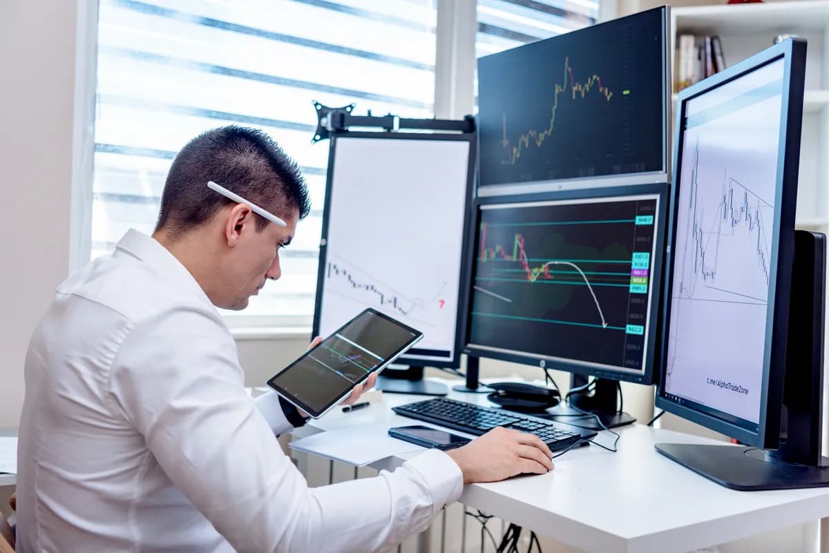 Trader en day trading suivant plusieurs écrans avec graphiques de marché en temps réel